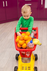 Cheerful little boy with shopping cart. Little kid in casual wear carrying child plastic shopping trolley. Shopping, discount, sale concept