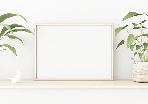 Horizontal poster mockup with golden metal frame standing on wooden table and decorated with green plants in basket on empty white wall background. 3D rendering, illustration.