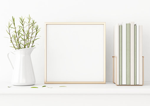 Square poster mockup with golden metal frame standing on table and decorated with jug, green plants and pile of books on empty white wall background. 3D rendering, illustration.