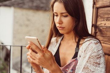 Attractive woman with a phone sits on the balcony.