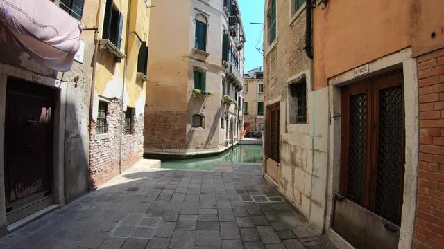 Venice, Italy-27 July, 2018: 4K. Walking through a typical street in the city of Venice, Italy. At the end of the street there is a canal. Subjective shot of a person walking.