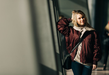 Photo of blonde in jacket standing against windows