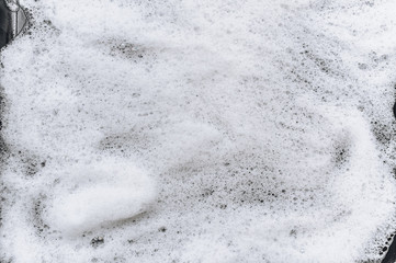 White foam and soap on black background. Abstract pattern. Car wash. Copy space.