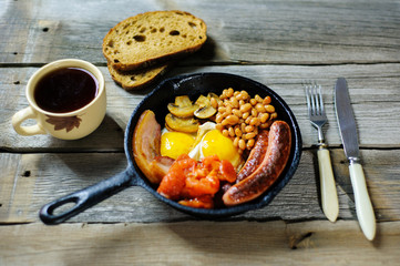 full irish breakfast with fried egg, sausages, black pudding, white pudding, baked beans, bacon, tomato and grilled mushrooms in a cast iron pan
