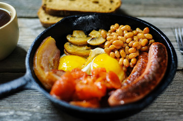 full irish breakfast with fried egg, sausages, black pudding, white pudding, baked beans, bacon, tomato and grilled mushrooms in a cast iron pan
