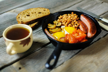 full irish breakfast with fried egg, sausages, black pudding, white pudding, baked beans, bacon, tomato and grilled mushrooms in a cast iron pan