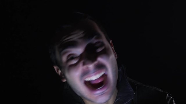 Crazy possessed man making weird faces with a strobe light flashing on his face.