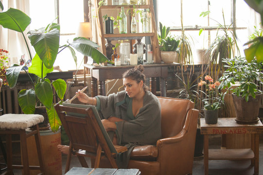 Woman wrapped in scarf painting on canvas while sitting by plants at home