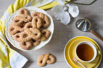 flat lay typical Dutch biscuit called Krakeling, on white cake stand. yellow cup of tea