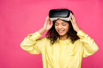curly african american woman wearing virtual reality headset and smiling isolated on crimson