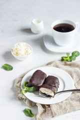 Glazed cheese curds with chocolate and mint on a white plate and a cup of coffee. Sweet breakfast or dessert. High key.