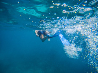 young man swimming and snorkeling with mask and fins in clear blue water