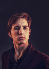 Obraz premium Portrait of an expressive, stylish, young man in a strict suit in orange tones with a smoky background