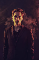 Obraz premium Portrait of an expressive, stylish, young man in a strict suit in orange tones with a smoky background