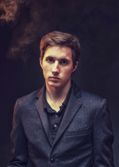 Portrait of an expressive, stylish, young man in a strict suit in orange tones with a smoky background