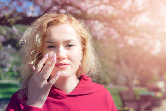 Young Woman Is Applying Sunscreen To Her Face While Sitting On The Bench In The Park.