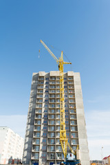 Fototapeta premium yellow tower crane and the construction of a multi-storey building against a blue sky
