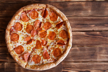 Sliced homemade pepperoni pizza lies on the natural wooden surface of pine boards