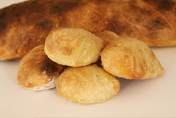 Just baked sourdough homemade buns lying in front of a bread of rustic quality on white background.