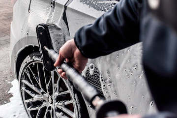 professionelle Autowäsche in einer Waschstraße- Mann reinigt den lack eines Fahrzeuges mit wasser...