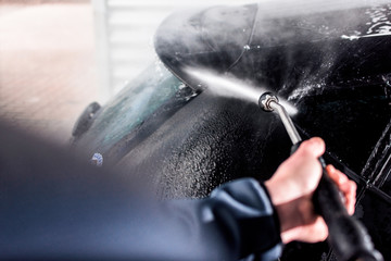 professionelle Autowäsche in einer Waschstraße- Mann reinigt den lack eines Fahrzeuges mit wasser...