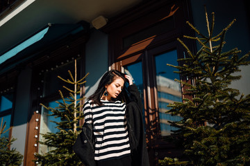 beautiful young brunette girl in black coat walking along city street, woman is relaxing outdoors