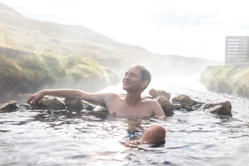 Young happy man bathing in Hveragerdi Hot Springs in Reykjadalur during autumn morning day in south Iceland on golden circle rocks and river steam