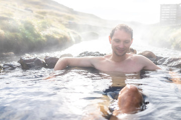Man bathing in Hveragerdi Reykjadalur Hot Springs during autumn morning day in south Iceland on golden circle rocks and river steam
