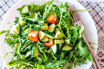 Closeup flat top macro of fresh raw chopped vegetable salad with arugula greens red tomatoes and cucumbers on table healthy lunch meal