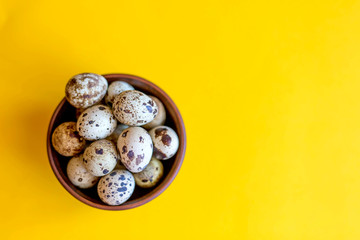 Quail Easter eggs in a wooden plate on a yellow background. Easter concept.
