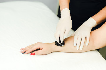 A beautician makes hair removal for clean, beautiful skin without hair. Depilation with black wax.