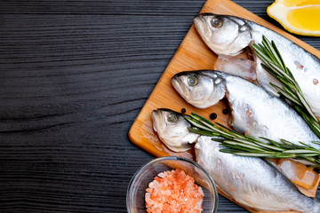 Raw fish with spices on black background.