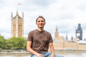 London, UK happy smiling man face sitting on railing by cityscape skyline of city with Thames River...