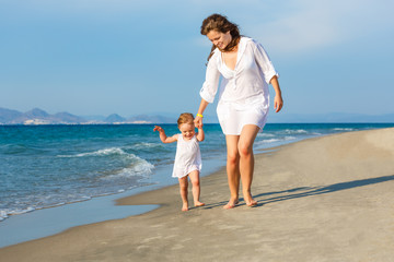 Mother and little daughter walking on the sea beach in Greece