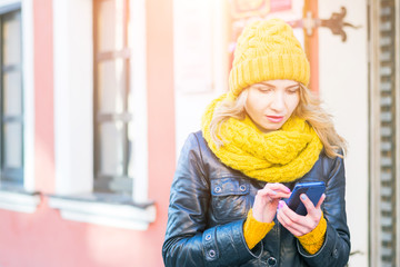 very attractive woman sms on her smartphone, smiles and looks into the camera, city street