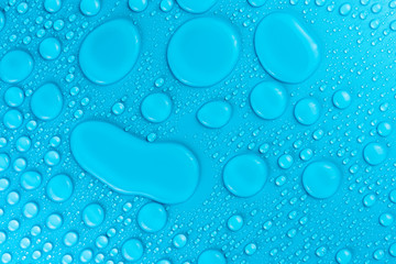 Droplets of water on a blue, matte background illuminated with a delicate light.