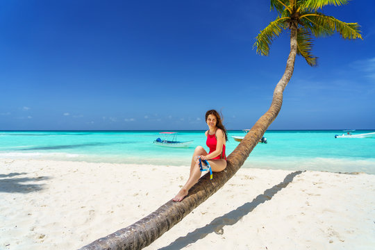 Young woman in bikini sitting on palm tree on the beach in Dominican Republic
