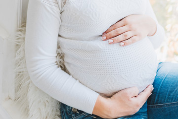 Beautiful caucasian pregnant woman wearing jeans and a white top. She is touching her belly. Pregnancy and expecting a baby.