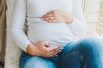 Beautiful caucasian pregnant woman wearing jeans and a white top. She is touching her belly. Pregnancy and expecting a baby.