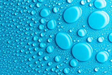 Droplets of water on a blue, matte background illuminated with a delicate light.