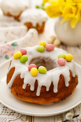 Easter yeast cake (Babka) covered with icing and decorated with marzipan eggs on a white plate on a wooden table. Traditional Easter cake in Poland