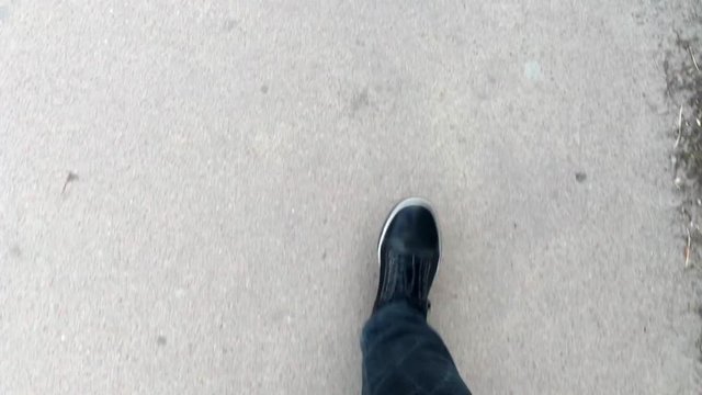 First person view of the feet of the guy who walks in sneakers on the asphalt.