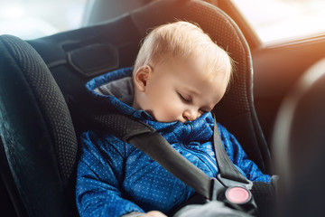 Cute caucasian toddler boy sleeping in child safety seat in car during road trip. Adorable baby...
