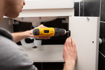 Worker installing doors on the closet. Furniture repair and assembly concept. Young man assembling bathroom furniture. Hands close up.  Carpenter working with screwdriver. - 257774745
