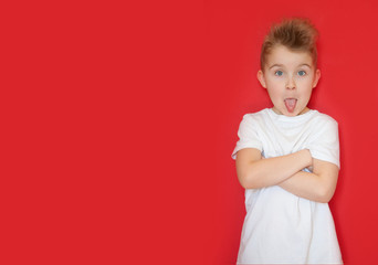 A little boy in a white shirt shows his tongue and makes faces. Red background.