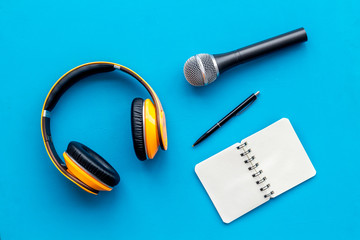 blogger, journalist or musician office desk with notebook, microphone and headphones on blue background top view copyspace