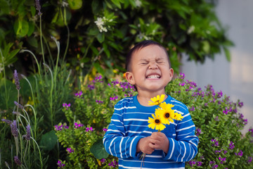 A cheerful young boy holding a few hand picked yellow flowers during spring time, standing in front...