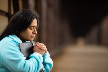Hispanic Woman Sitting On A Bridge Praying While Holding Bible