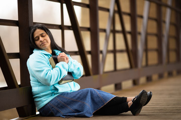 Obraz na płótnie Canvas Hispanic Woman Sitting On A Bridge Praying While Holding Bible