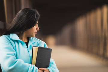 Hispanic Woman Praying While Holding Bible On A Bridge